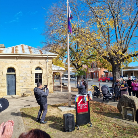 Cr Price raising the rainbow flag in front of large crowd outside historic courthouse