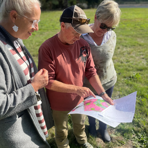 Two women and a man look over development plans in a green field